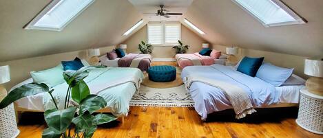 A cozy attic bedroom with two beds, a ceiling fan, and skylights.