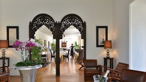 A hotel lobby with a central walkway, wooden chairs, a silver vase with flowers, and a table with a champagne bottle and glasses. - La villa (Antibes)