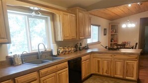 A kitchen with wooden cabinets, a dishwasher, and a window providing natural light. - Pine Mountain Retreat (Ruidoso)