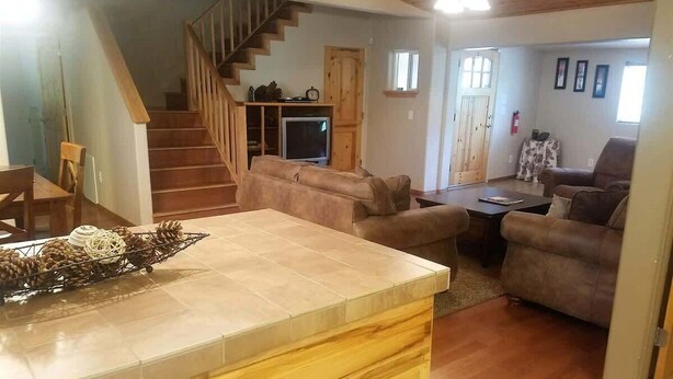 A spacious living area with a wooden staircase, a fireplace, and a television. - Pine Mountain Retreat (Ruidoso)