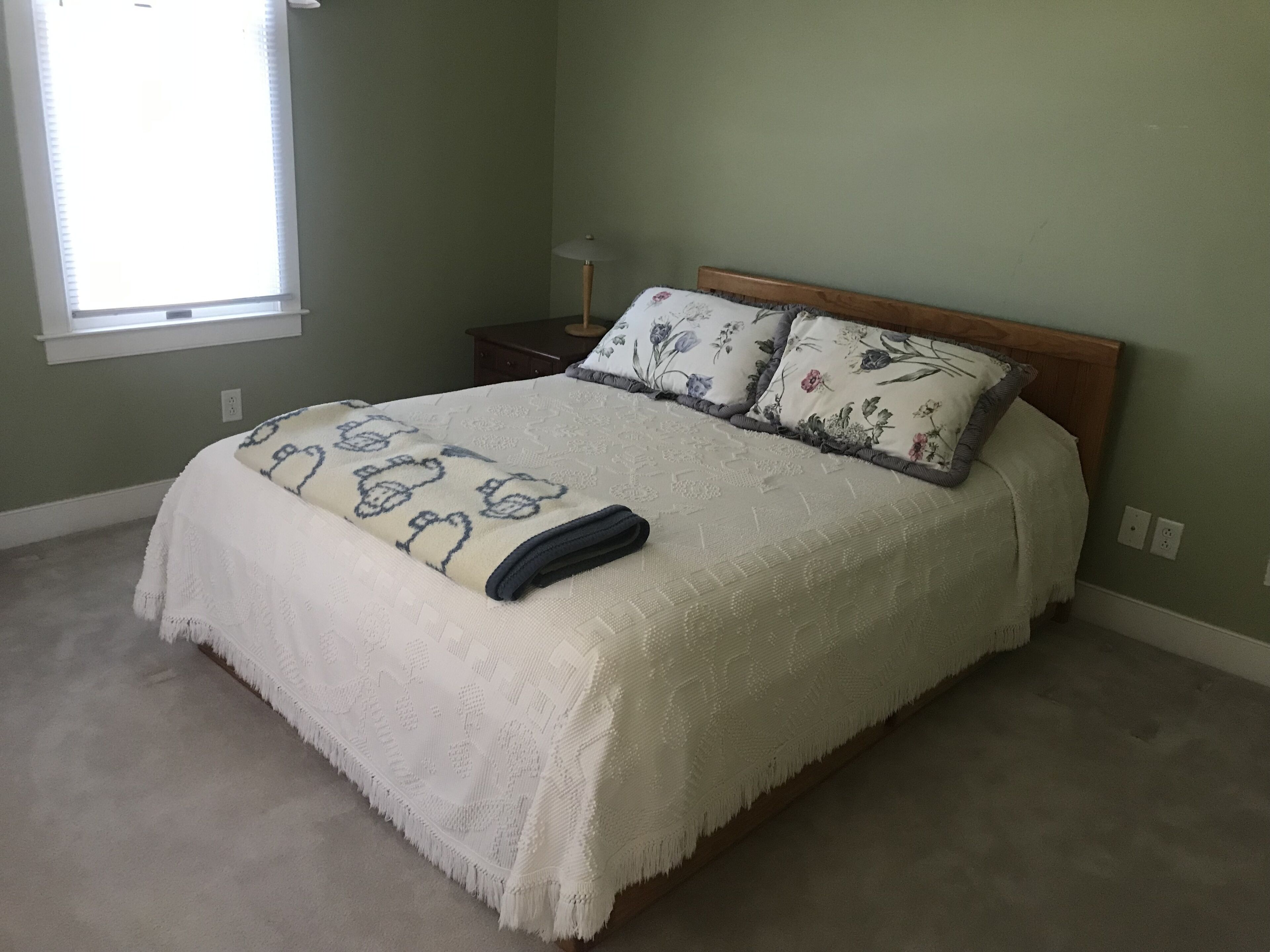 Een slaapkamer met een bed, nachtkastje, lamp en raam.