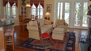 Un salón amplio con un sofá grande, un sillón mecedora y una zona de comedor con mesa y sillas.