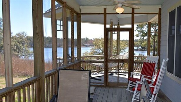 Una terraza de madera con vistas a un lago, un ventilador de techo y dos mecedoras.
