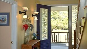 Un pasillo con un banco de madera, una puerta con un panel de vidrio decorativo y una escalera a la derecha.