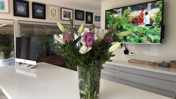 A modern living room with a flat-screen TV mounted on the wall, a large white table, and a vase with flowers. - Supersized whole floor Residence Near Manly (Balgowlah)