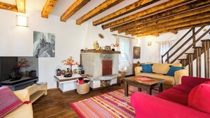 Una sala de estar acogedora con vigas de madera, una chimenea de piedra, un sofá rojo y un televisor sobre un mueble de madera.