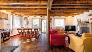 Amplia sala de estar con vigas de madera, chimenea, televisor y zona de comedor con sillas y mesa.