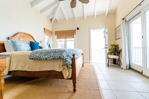 A bedroom with a wooden bed, patterned bedding, a woven rug, and a view through a door to a balcony. - SPECTACULAR OCEAN FRONT VILLA     (charlotte amalie)
