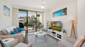 Una sala de estar moderna con sofá, televisión y un balcón con parrilla.
