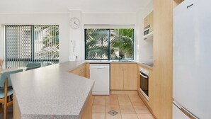 Een moderne keuken met een centraal eiland, houten keukenkastjes en uitzicht op palmbomen.