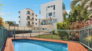 Edificio residencial con piscina, rodeado por una valla y palmeras.