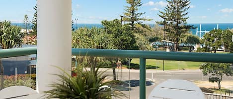 Un balcon donnant sur une route, des arbres et un bâtiment, avec une éolienne en arrière-plan.