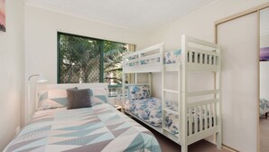 Een kamer met een stapelbed, een bureau en een raam met uitzicht op bomen.