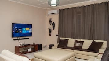 Una sala de estar con un televisor de pantalla plana, un sofá, una mesa de centro y un adorno de pared.