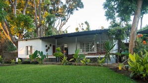 A single-story house with a flat roof, surrounded by a well-maintained lawn and various tropical plants.