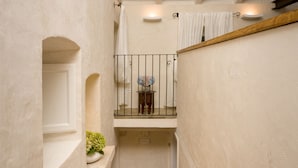 En smal trappe med trætrin fører op til en balkon med gelænder og et lille bord med en vase.