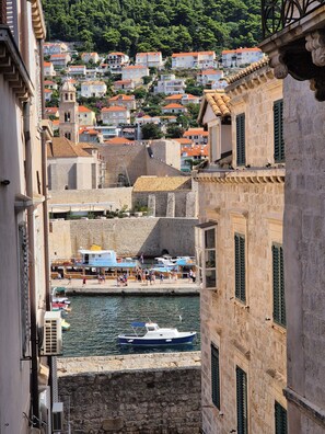 Une rue étroite bordée de bâtiments des deux côtés, un quai avec des bateaux et une colline parsemée de maisons.