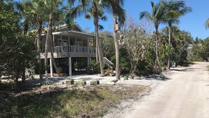 A two-story house with a balcony, surrounded by palm trees and a gravel driveway.