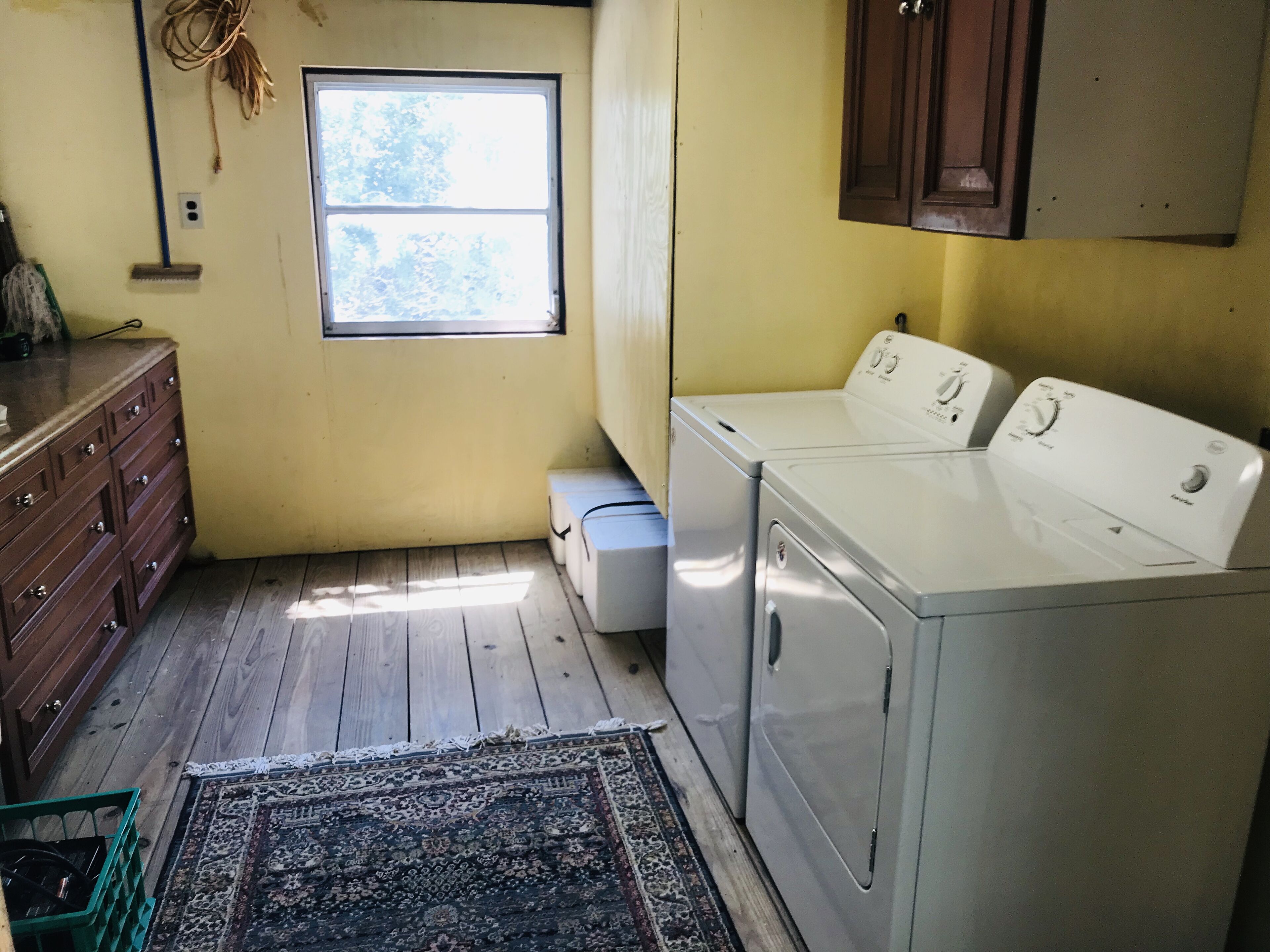 A laundry room with a washing machine and dryer, wooden floor, a window, and a cabinet.