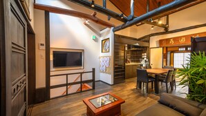 A modern interior with a wooden floor, a glass-top coffee table, a sofa, a dining area with chairs, and a kitchen area with a stove. - Miyagawacho Samurai Machiya, Miyagawacho Samurai Machiya (京都市)