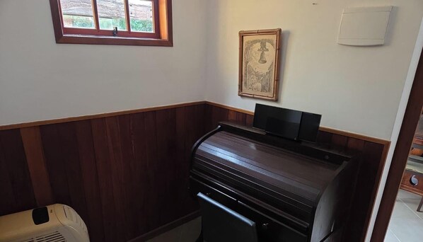 A room with a piano, a radiator, a framed picture on the wall, and a window with a view of greenery. - Property in Areal, 15 minutes from the center of Itaipava and Itaipava Castle. (Areal)