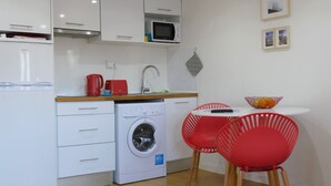 A compact kitchen with white cabinets, a microwave, a washing machine, and a small dining area with red chairs and a white table. - St Clara House-My Studio. Enjoy, visit or work @Graça (Lisboa)
