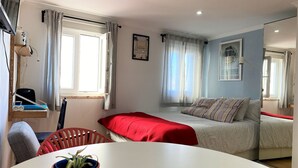 A modern bedroom with a bed, a desk, and a chair. There is a window with curtains, a plant on the desk, and a framed picture on the wall. - St Clara House-My Studio. Enjoy, visit or work @Graça (Lisboa)