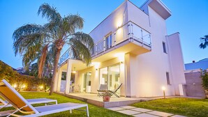 A modern two-story house with a balcony, a patio with lounge chairs, and a well-maintained lawn. - New elegant Villa EMANUELE in Mondello Beach (Palermo)