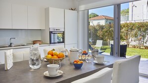 A modern kitchen with white cabinets, a dining table set with tea cups, a pitcher, and a bowl of oranges. - New elegant Villa EMANUELE in Mondello Beach (Palermo)