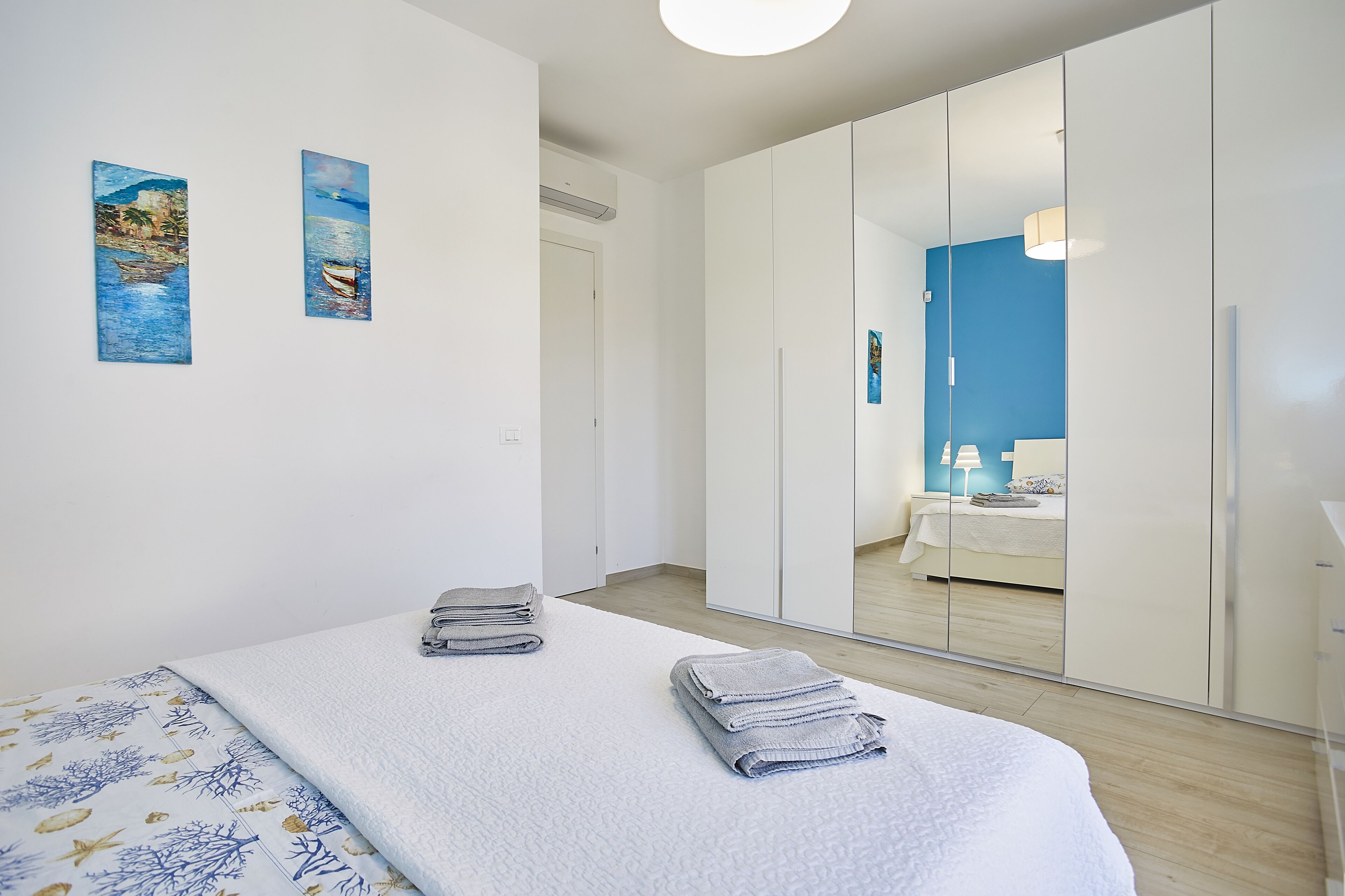 A bedroom with a bed, two towels, a nightstand, a mirror, and artwork on the wall.