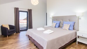A modern bedroom with a large bed, a sofa, and a view through a glass door. - Endless Blue House view of the ocean with a huge pool (Arco da Calheta)