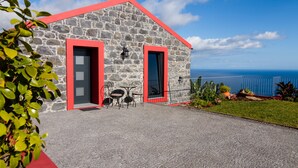A stone building with red trim, a small patio with tables and chairs, and a view of the sea. - Endless Blue House view of the ocean with a huge pool (Arco da Calheta)