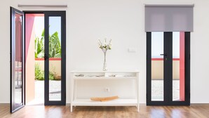 A room with a white console table, a vase with flowers, and a view of a garden through a sliding door. - Endless Blue House view of the ocean with a huge pool (Arco da Calheta)