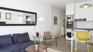 A modern living room with a sofa, a round table, a chair, and a kitchen area with appliances. - Always Easy I San Blas (San Sebastián/Donostia)