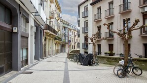 A narrow urban street with buildings on both sides, bicycles parked along the sidewalk, and a tree with bare branches. - Always Easy I San Blas (San Sebastián/Donostia)