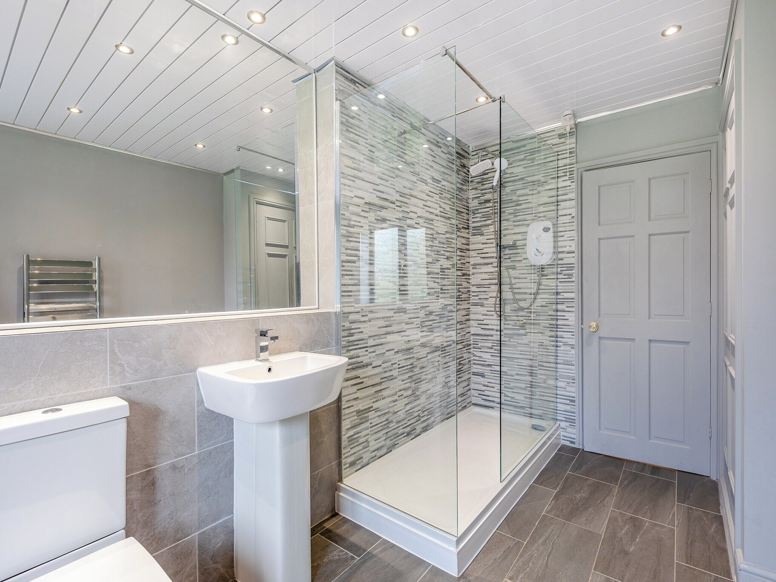 A modern bathroom with a glass-enclosed shower, a white pedestal sink, and a large mirror.