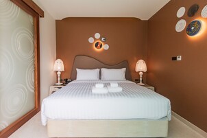 Una habitación de hotel con una cama grande, dos mesitas de noche, una lámpara fijada a la pared y un panel decorativo.