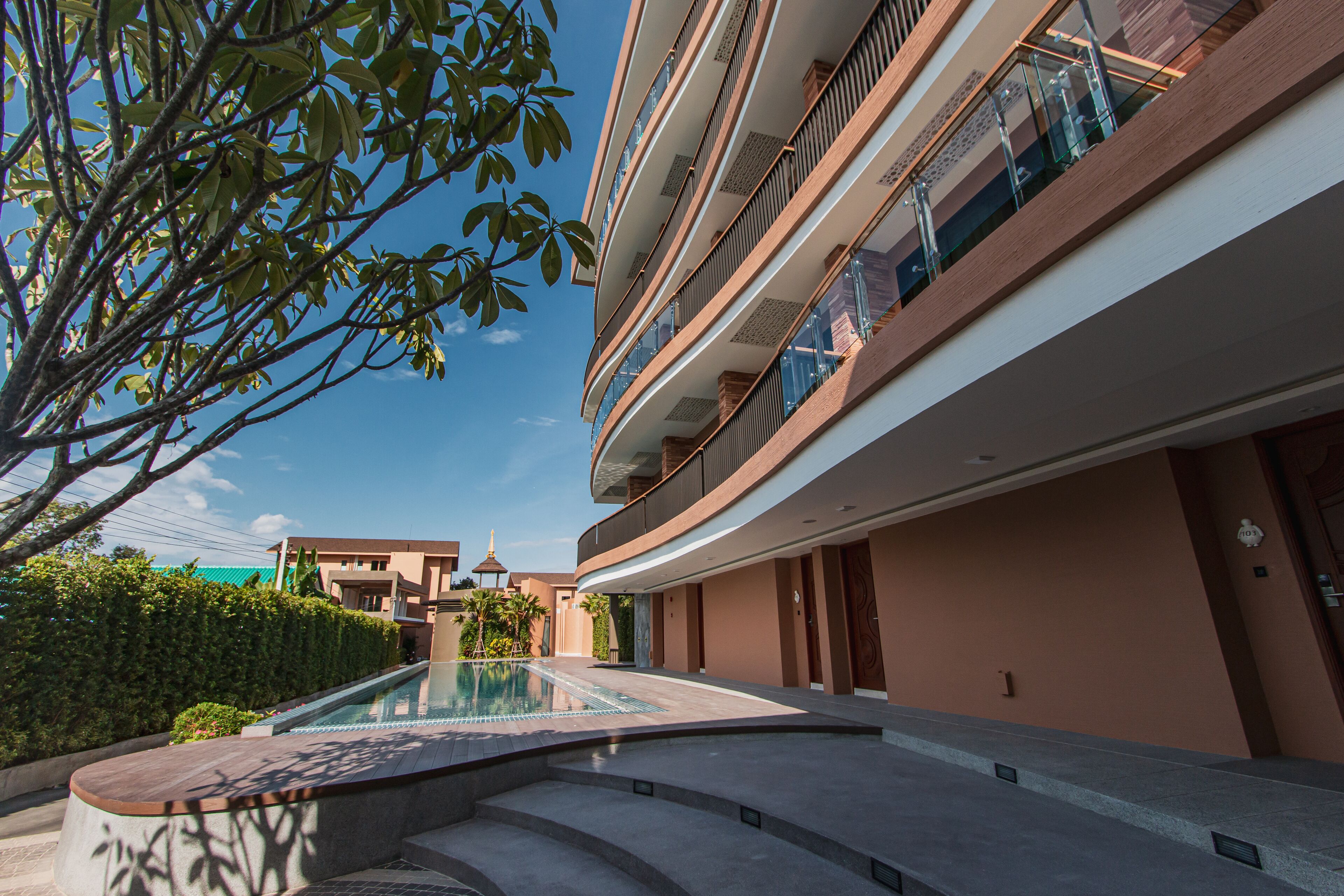 A modern hotel with a swimming pool, multiple balconies, and a clear sky.