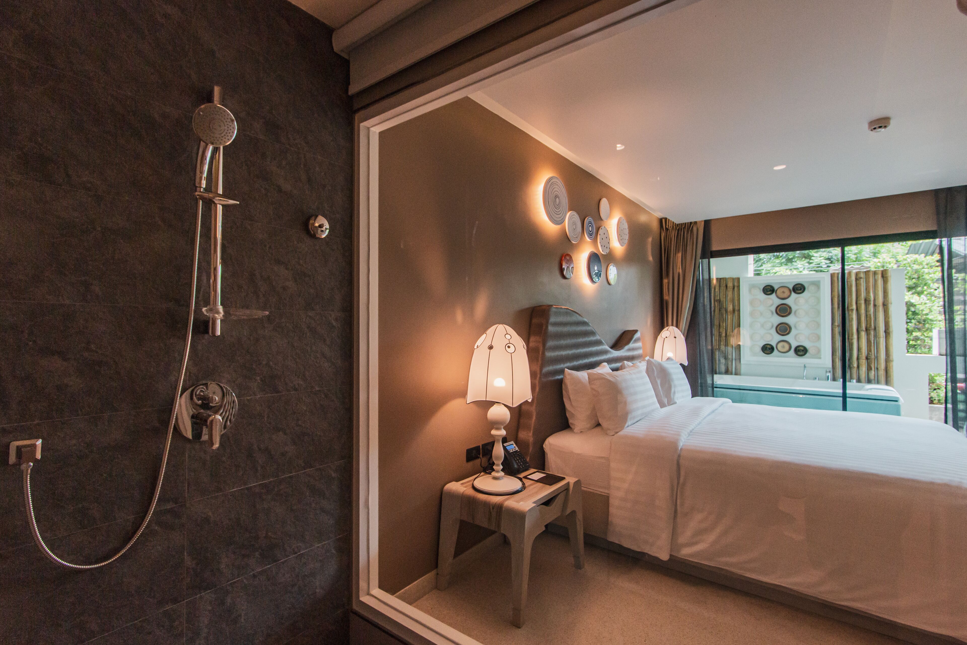 A modern hotel room with a large bed, a bedside table with a lamp, a shower, and a wall with decorative plates.