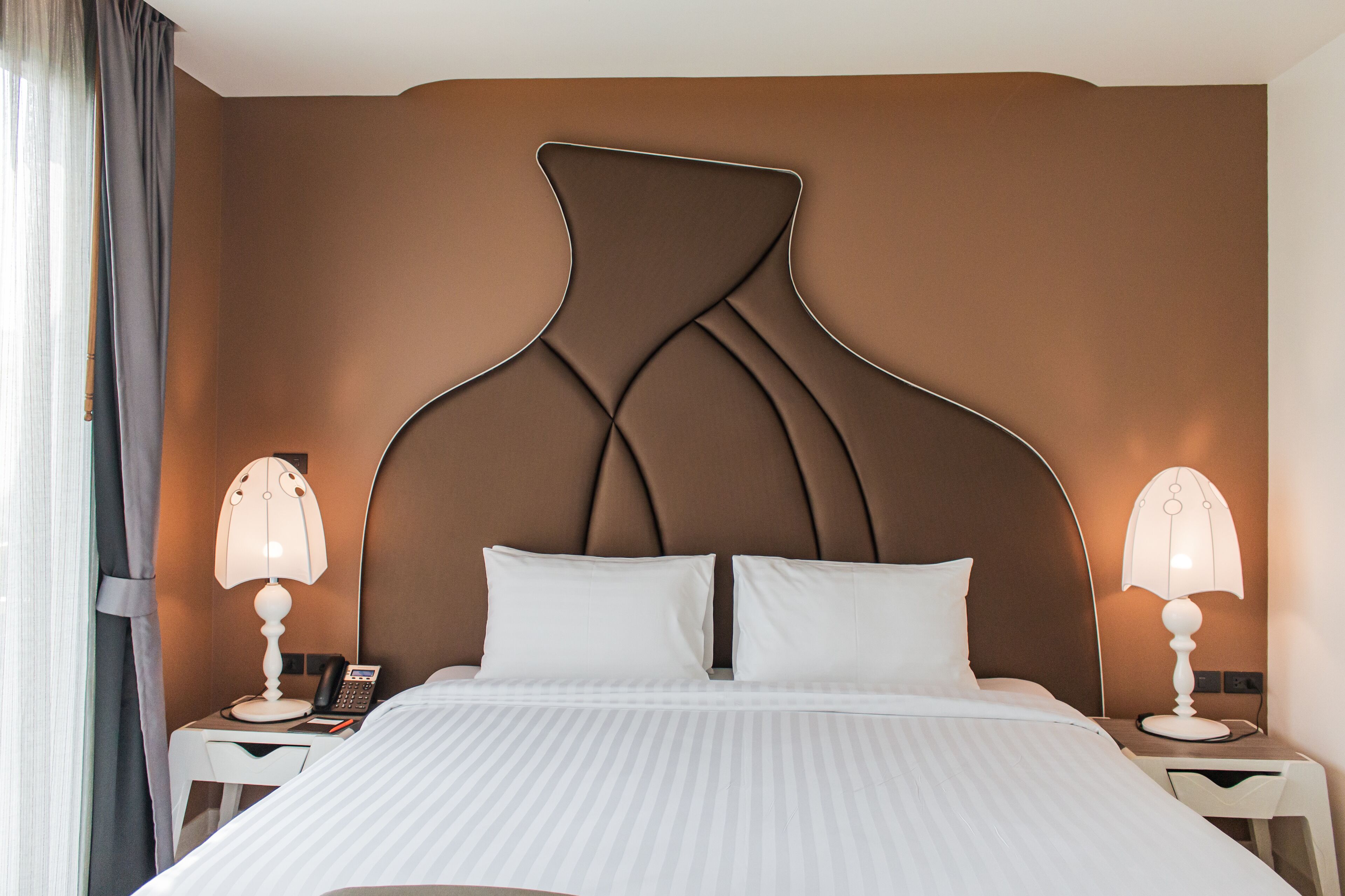 Une chambre d’hôtel dotée d’un lit moderne, de deux tables de chevet avec des lampes et d’une tête de lit au design original.