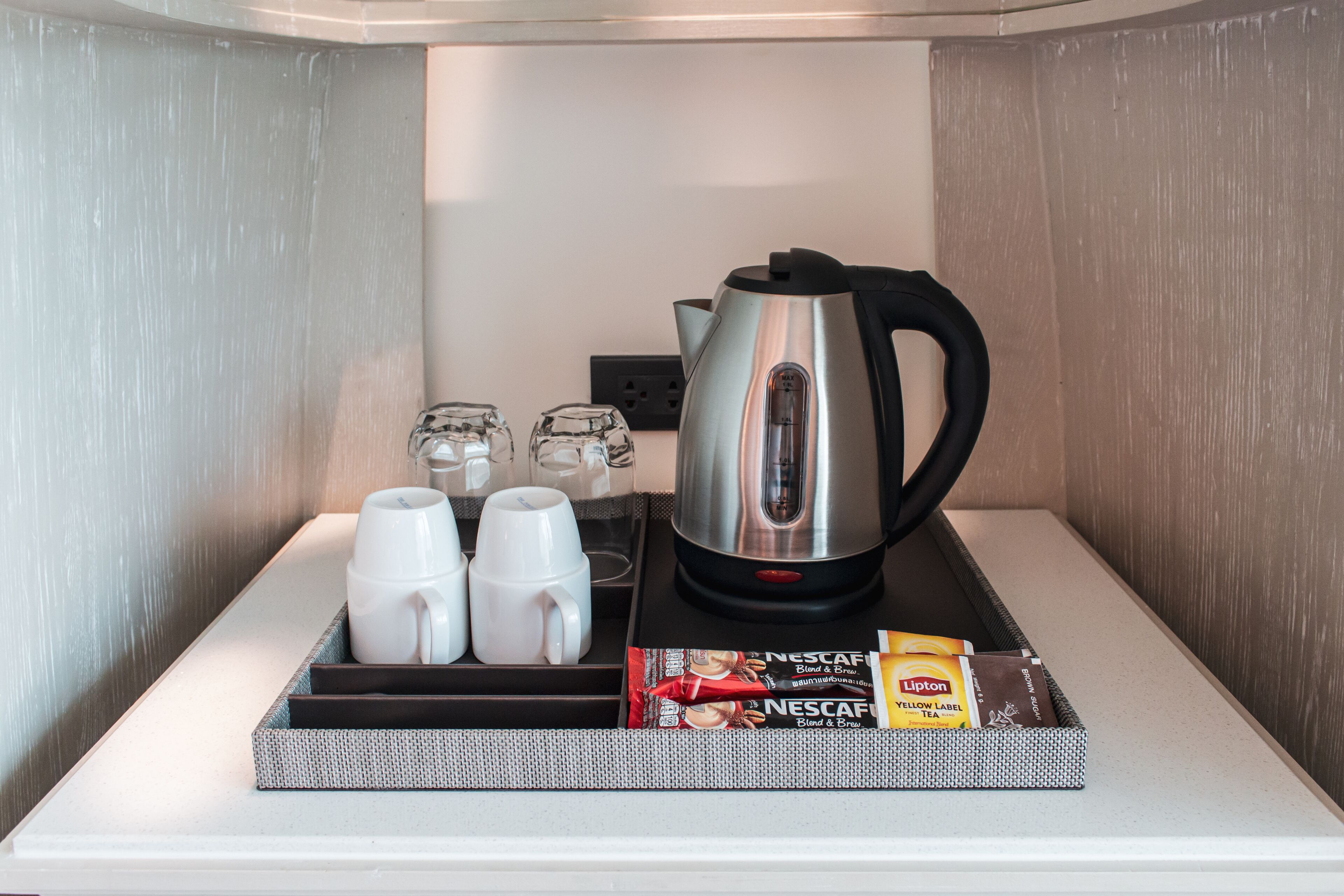 Una kitchenette con cafetera, dos tazas, una bandeja y una caja de café instantáneo Nescafé.