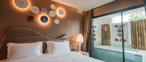 A hotel room with a large bed, a bedside table with a lamp, and a view of a pool area through a glass door.