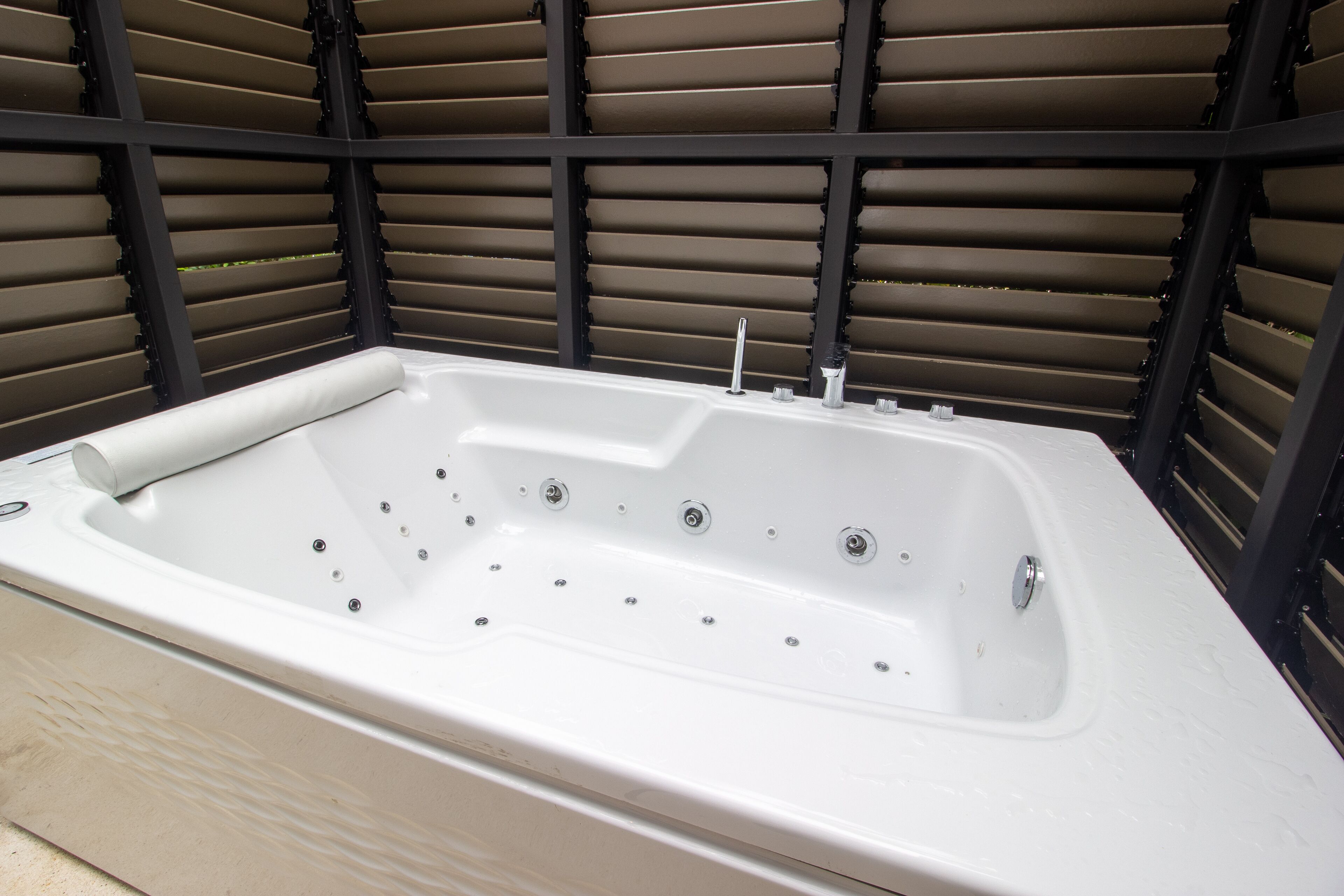 A white freestanding hot tub with multiple jets, positioned against a backdrop of horizontal slats.