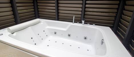 A white freestanding hot tub with multiple jets, positioned against a backdrop of horizontal slats.