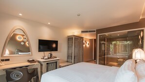 Una habitación de hotel moderna con una cama grande, un escritorio con una silla, un televisor y un vidrio que da a un balcón.