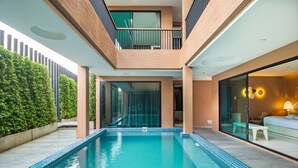 Un área de piscina moderna con vista despejada, una puerta de cristal que da a un balcón y un espacio de descanso con sofá y mesa.