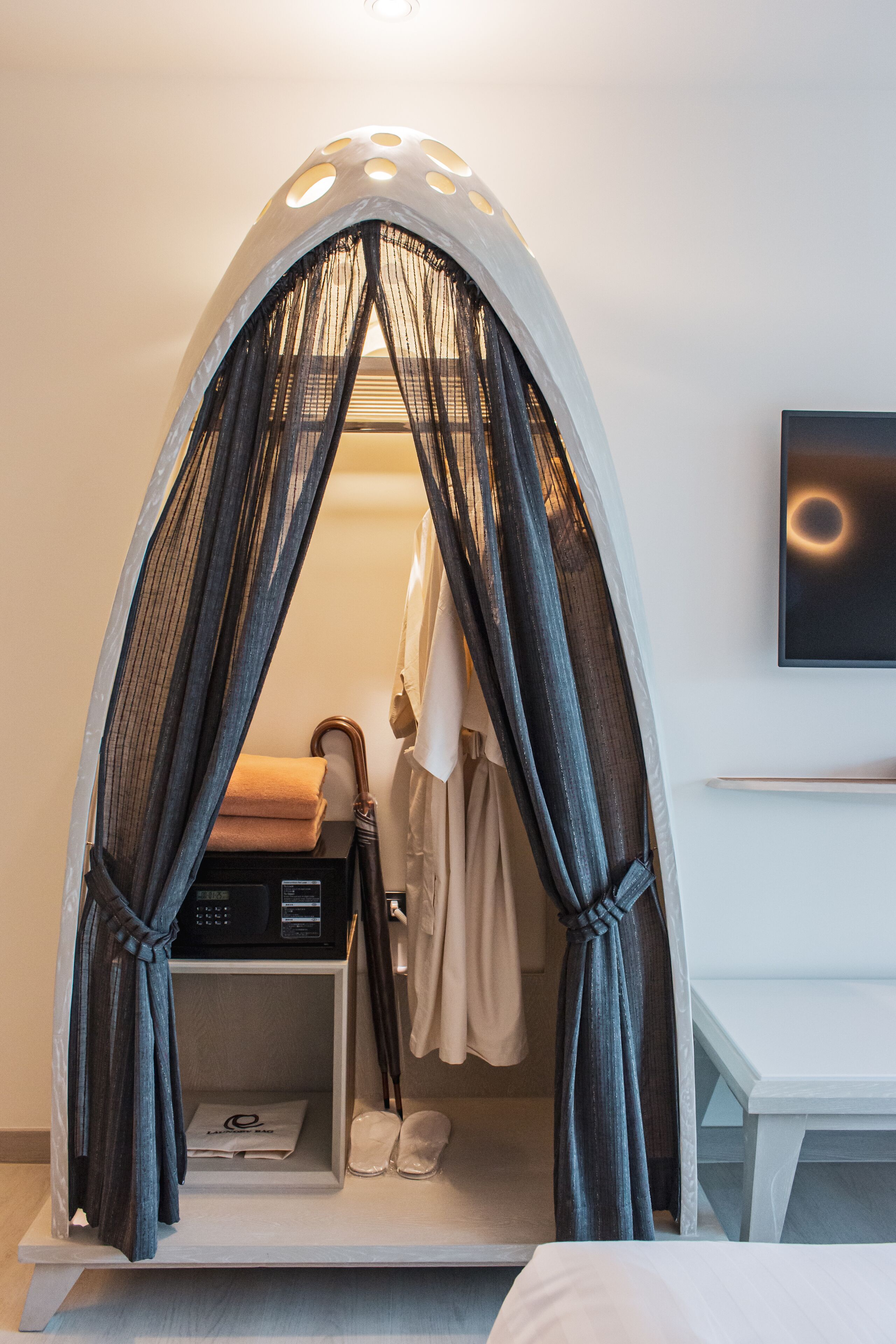 A room with a canopy bed, a TV mounted on the wall, and a desk with a chair.