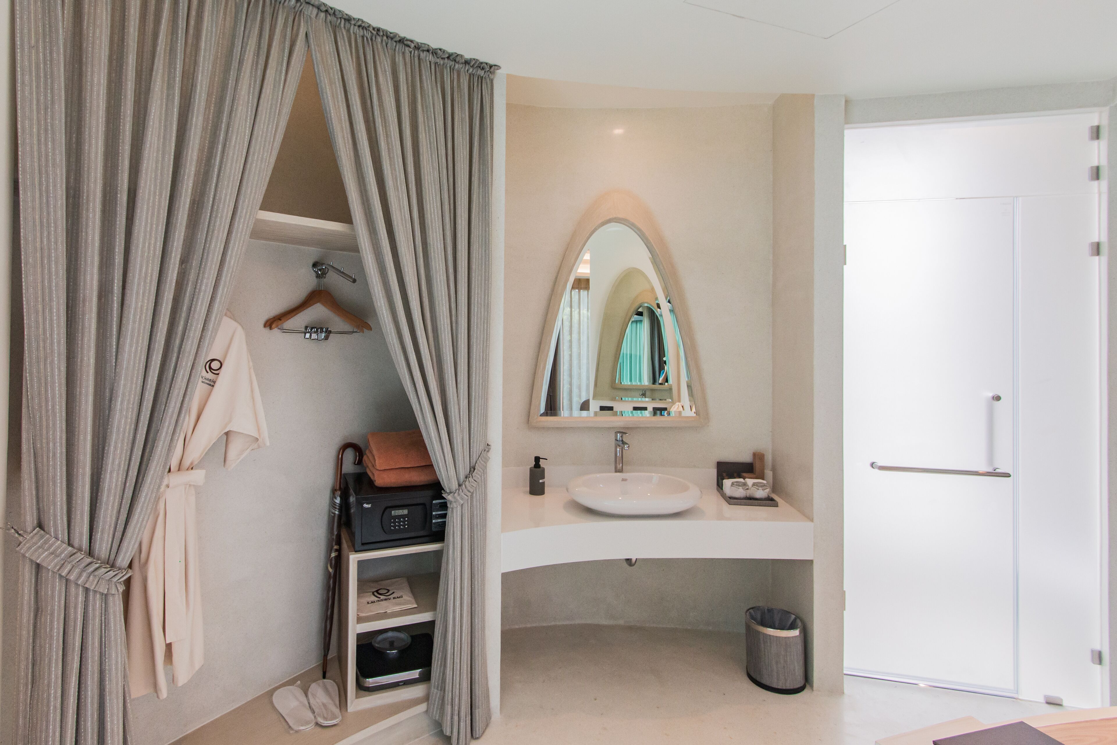 A modern bathroom with a vanity, a large mirror, a hanging robe, and a shoe rack.