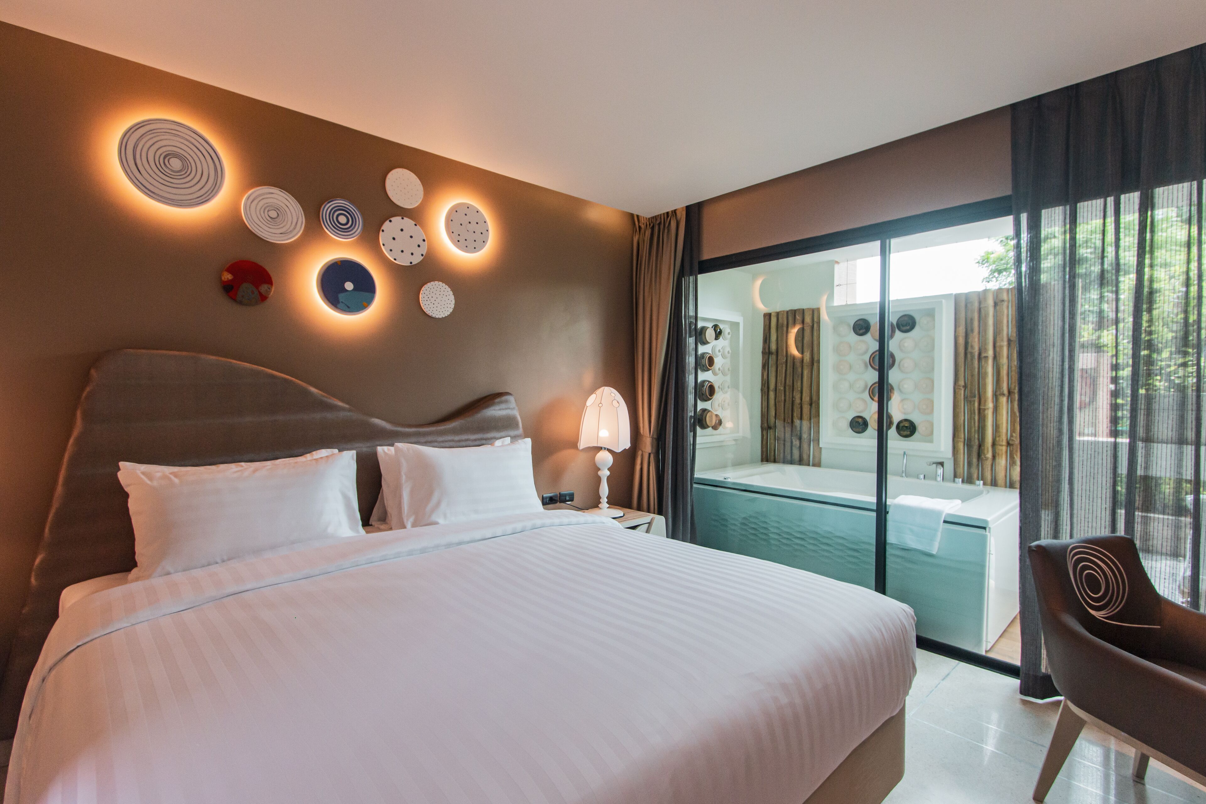 Ein modernes Hotelzimmer mit einem großen Bett, einer Sitzecke und Blick auf einen Spa-Bereich.
