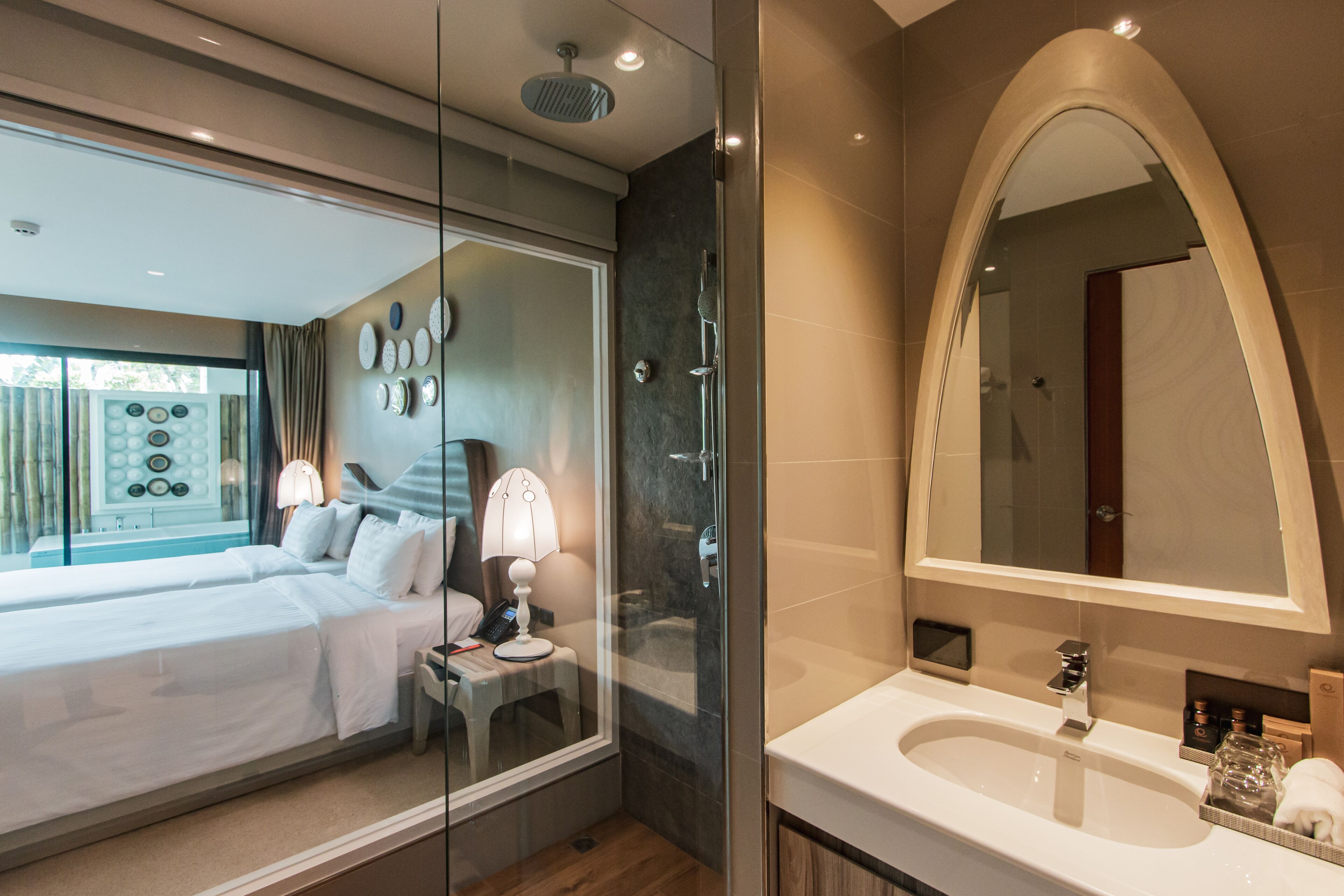 Una habitación de hotel moderna con una cama grande, un box de ducha de vidrio, un espejo amplio y un baño con lavamanos y tocador.